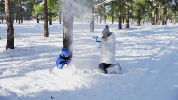 Little Boy in Blue Jacket and His Mother Plays with Snow in Winter Park