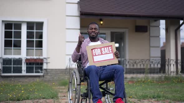Confident Cheerful African American Disabled Sales Agent in Wheelchair Advertising House Pointing at