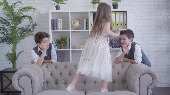 Little Cheerful Caucasian Girl Jumping on Couch and Stretching Boy's Hand. Joyful Sister