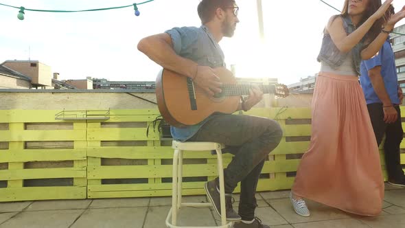 Handsome musician playing guitar, young people dancing at the rooftop party
