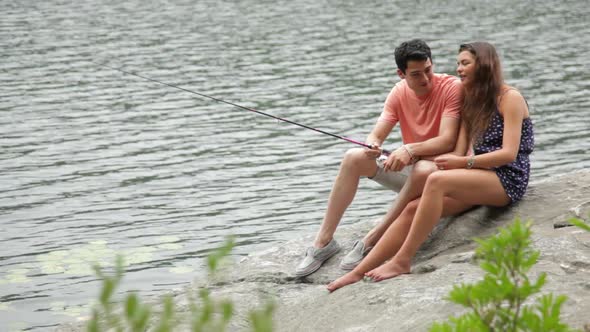 Young couple fishing from rock at lakeside