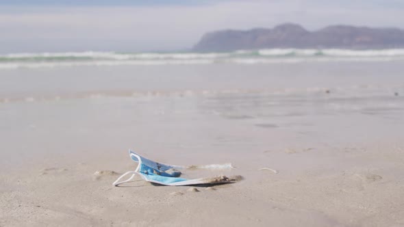 A face mask lying in sand on the beach with waves in the background