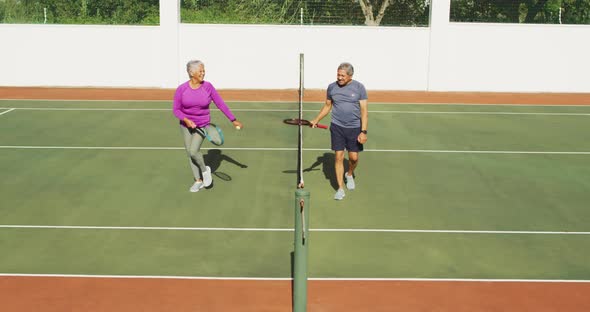 Video of happy biracial senior couple walking after match on tennis court