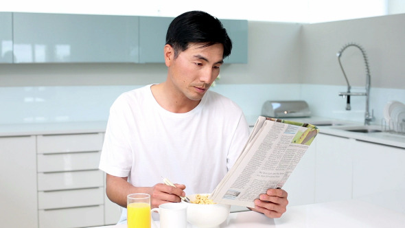 Attractive Man Eating Cereal And Reading Magazine