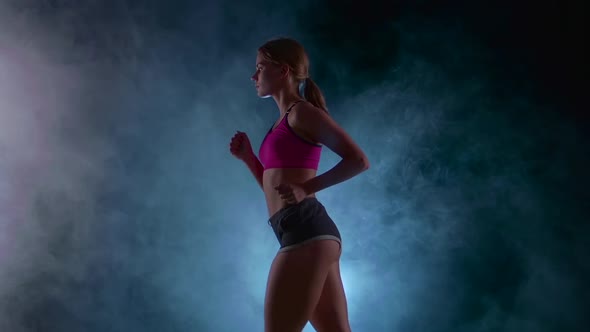 Athletic Fitness Girl Running on a Black Background Illuminated By the Spotlight in the Smoke