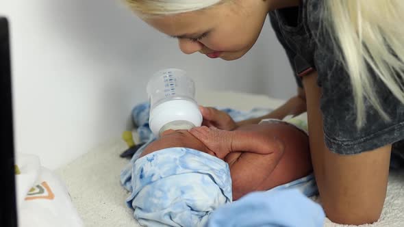 Anonymous mother feeding newborn baby wrapped on soft blanket