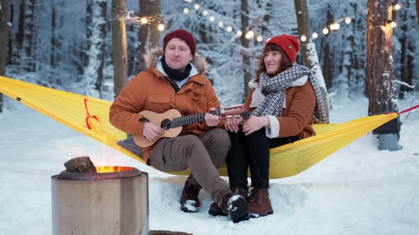 Couple Guy with a Girl Sitting By the Fire with a Singing Fun with a Guitar Winter