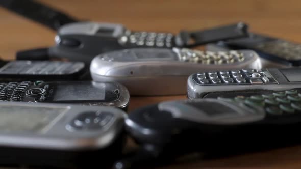 Old broken scratched and dusty cell phones lie in pile on table.