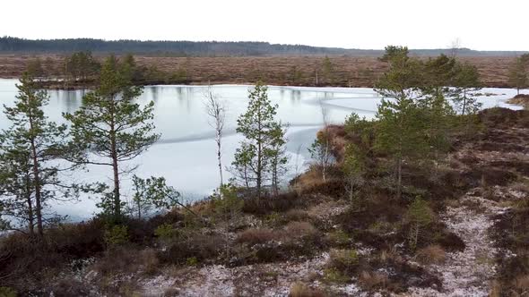 Aerial drone view of a frozen bog lake with the barren and empty landscape around it. Recorded in Lu