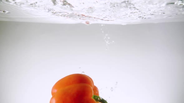 Orange Bell Pepper Falls Down in Clear Water with Bubbles