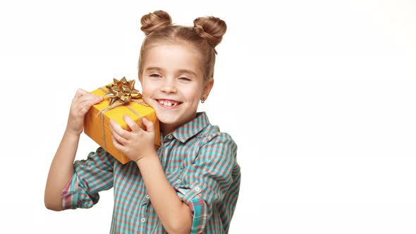 Young Adorable Caucasian Kid Girl Standing on White Background and Holding Yellow Box with Gift in