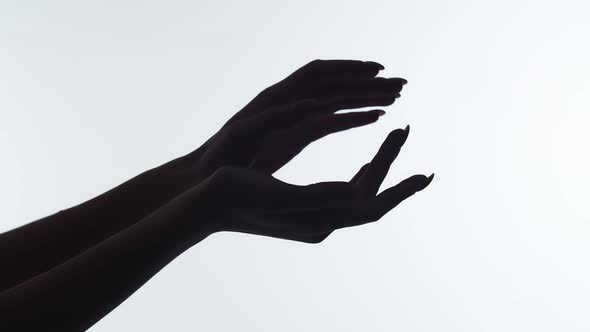 Closeup of the silhouette of woman's hands on white background, runs finger along arm after applying