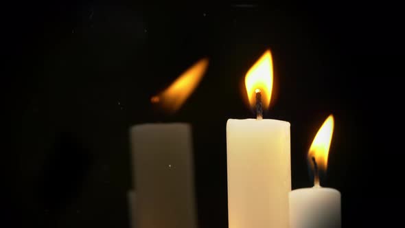 White Paraffin Candles with a Yellow Tint Burn on Black Background in Reflection