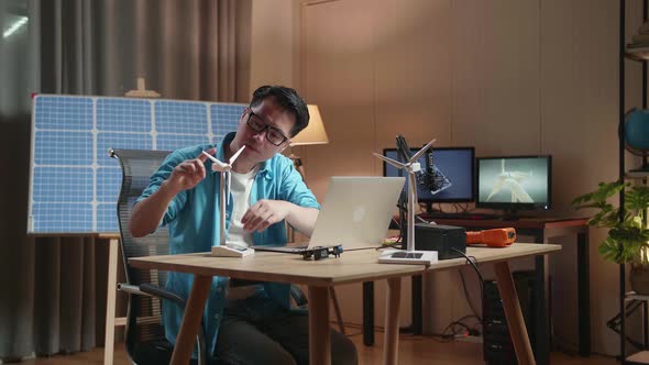 Asian Man Assemble The Wind Turbine While Working With Laptop Next To The Solar Cell At The Office