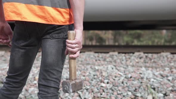 The railway man stands near the railroad with a sledgehammer. Railroad maintenance concept.