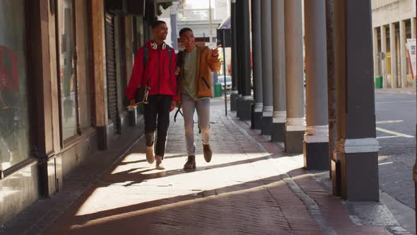 Two happy mixed race male friends walking and talking in the street