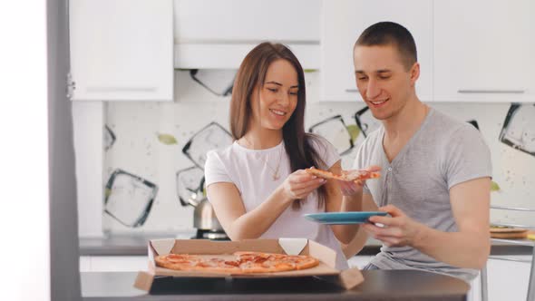 Young Happy Couple Opening Box and Putting Pizza to the Dish