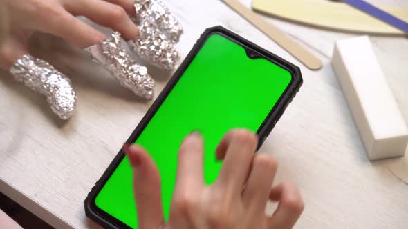 A Girl During a Manicure Uses a Smartphone with a Green Screen