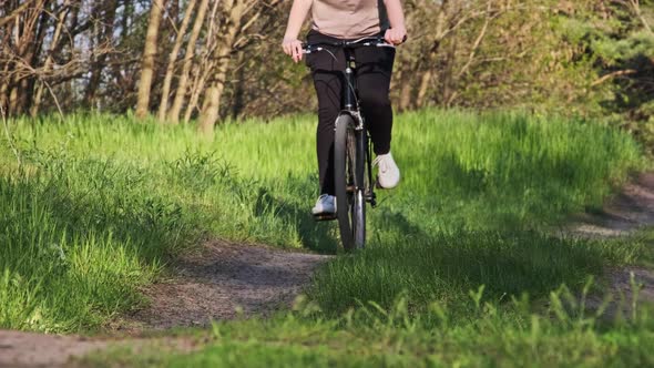 Woman on Bicycle Rides Along Forest Path in a Green Area on a Sunny Summer Day