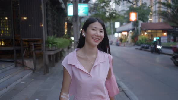 Cute Girl Walking Happily on the Street with Headphones on Her Ear and a Bag on Her Shoulder