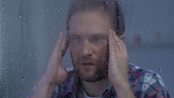 Depressed Man Suffering Strong Migraine, Massaging Temples, Looking at Rain
