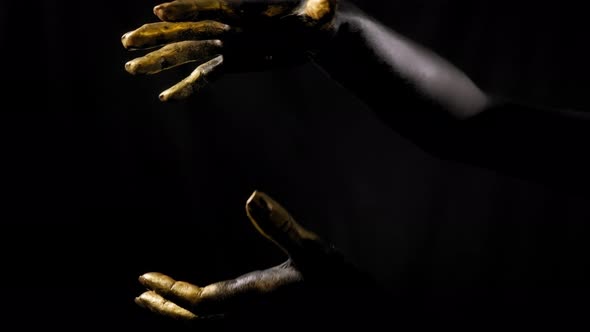 Closeup of the Black Hands of a Woman with Golden Fingers on a Black Background