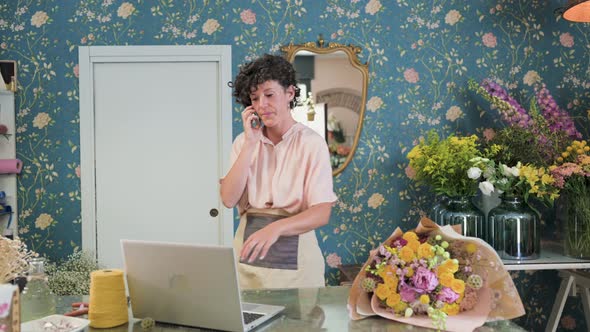 Smiling florist getting order and talking on smartphone in flower shop