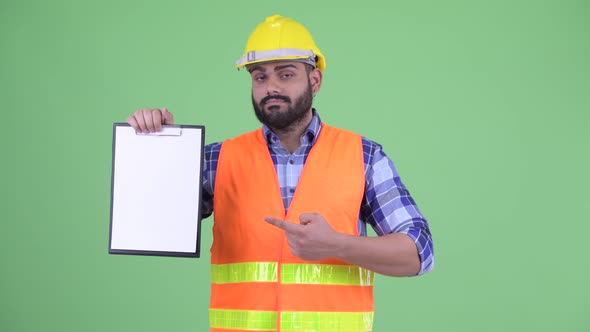 Stressed Overweight Bearded Indian Man Construction Worker Showing Clipboard and Giving Thumbs Down