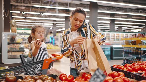 Busy Mom in the Supermarket Talking on the Phone and Putting Tomatoes in a Paper Bag