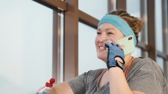 Overweight Woman in Modern Gym at Window Holding Smartphone