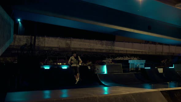 Active Teen Riding Scooter on Ramp at Night Skate Park