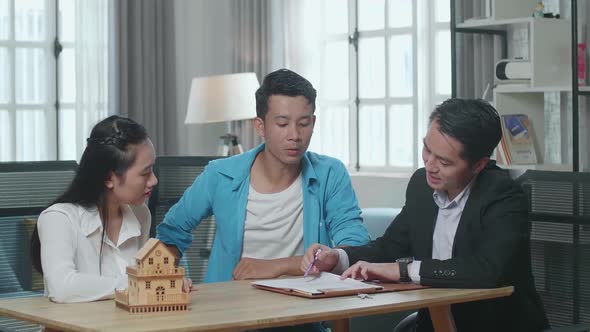 Asian Real Estate Agent Explaining About House Purchase Contract To A Couple At The Office
