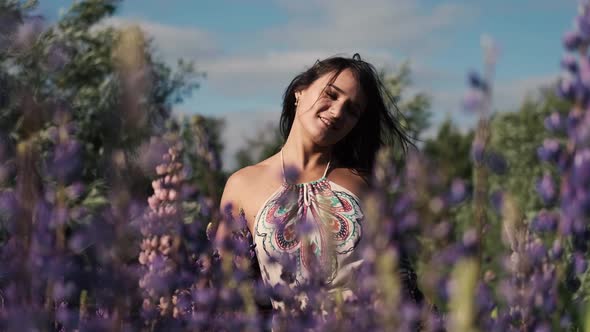 Young Beautiful Smiling Woman with a Bouquet Walks Among the Flowers of Purple Lupins