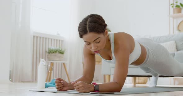 Young Lady Turning on Stopwatch on Her Fitness Tracker, Practicing Plank Workout at Home