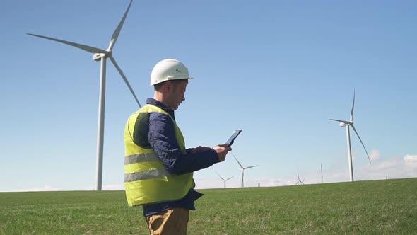 Technician Standing Near Wind Mill and Monitoring System on Tabl