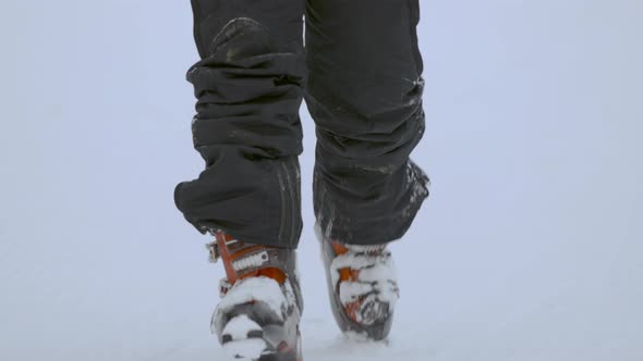 Feet in Ski Boots Go Through Deep Snow Towards the Camera