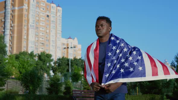 Patriot Afroamerican Man Walking Street with American Flag on Back in Summer