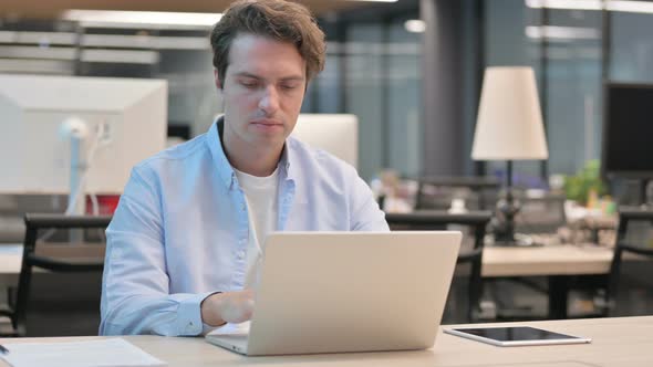 Man Showing Thumbs Down Sign While Using Laptop at Work