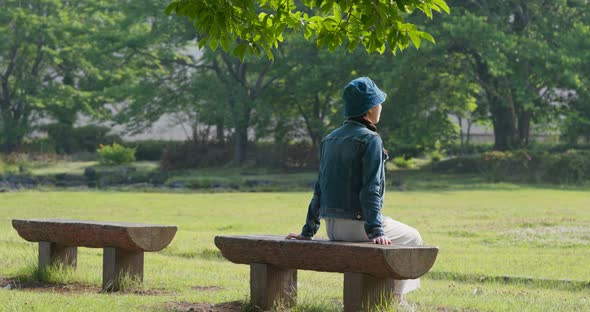 Woman sit on the wooden bench and look around in the park