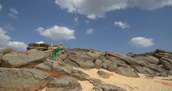 Sunny Day on a Rocky Shore Young Lady in Green Dress is Doing Yoga Poses