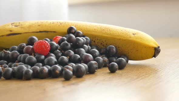 Fresh Organic Berries Black Currant and Raspberry and Banana on a Wooden Table