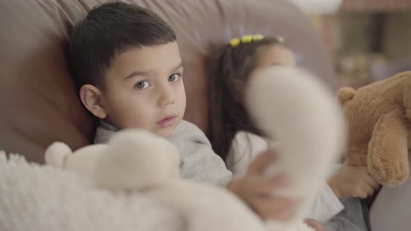 Close-up Face of a Cute Middle Eastern Boy Sitting with His Sister at the Coach and Playing Toys