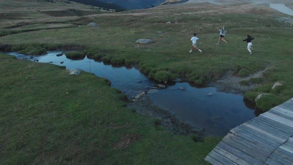 Aerial drone shot of friends running, raising hands and jumping through a mountain valley in the eve