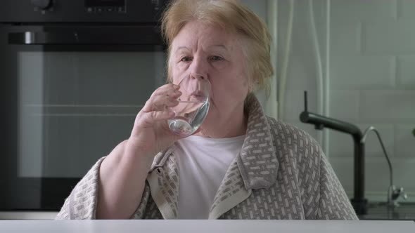 Elderly Woman Drinking Water From a Glass in the Kitchen at Home