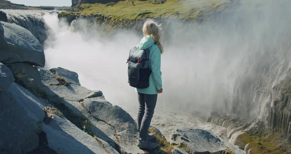 Woman Standing at Cliff Edge Looking at Powerful Detifoss Waterfall in Iceland