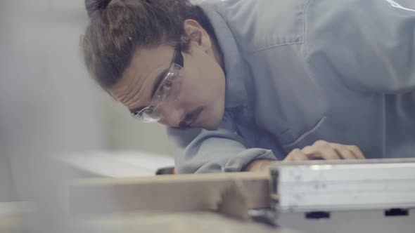 Young Carpenter Positioning Piece of Wood on Table Saw at Workshop