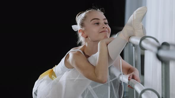 Flexible Ballerina Girl Child in Ballet Tutu Stretches Near Barre in Dance Class Stretching Legs