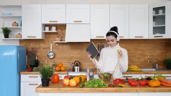 Young Woman Using Tablet Computer Following Recipe To Cook Salad In Her Kitchen.