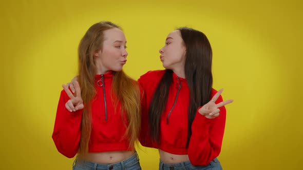 Front View Two Young Beautiful Coquette Women Posing at Yellow Background Gesturing Peace Gesture