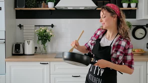 Carefree happy young woman housewife dancing alone cooking meal